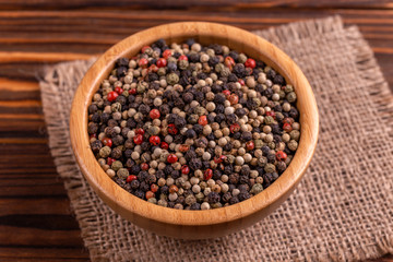 Mix of peppers in bowl burlap napkin on wooden background