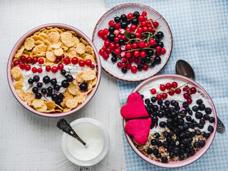 Festive and healthy breakfast for loved ones. Cereal biscuits in pink glaze, vintage bowls, cornflakes, granola, yogurt, fresh berries. Close-up, top view. Concept of healthy and delicious food