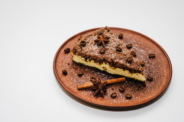 A piece of delicious chocolate cake with cream, coffee beans on a brown plate is isolated on a white background. Cinnamon, anise. happy holidays concept. Side view.