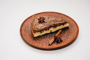 A piece of delicious chocolate cake with cream on a brown plate is isolated on a white background. Cinnamon, anise. happy holidays concept. Side view.