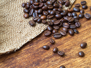Roasted coffee beans on burlap and wooden background, close up