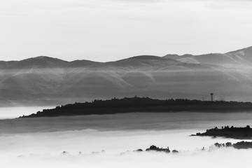 Fog filling a valley in Umbria (Italy), with layers of mountains and hills, trees in the foreground and Montefalco town at the distance