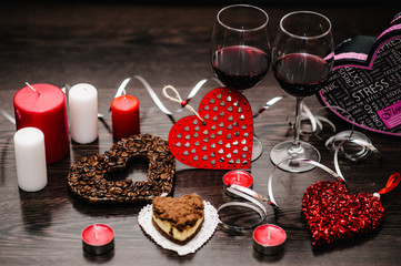 A romantic dinner, candles, concept of St. Valentine's Day. Cake, glasses of wine. heart with coffee beans. Decorated red hearts on brown wooden background. composition love. space for text. side view