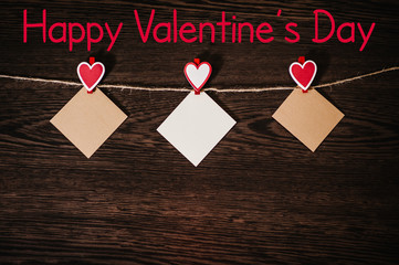 Text happy Valentine's Day. Craft paper, three blank, with red heart hanging on lacing, rope on brown wooden background with space. Place for text. concept International Women's Day, eighth of March.