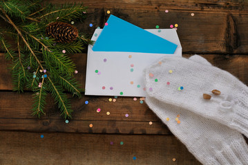 New Year and Christmas card. White paper envelope, fir branches, confetti and warm homemade mittens on an old wooden background.