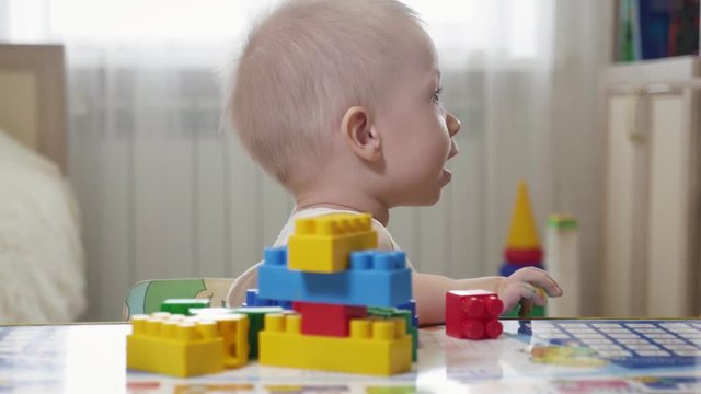 Little baby boy playing with colourful small blocks of a constructor in the room on the floor. Kid playing with colored blocks of a constructor on floor in children room.