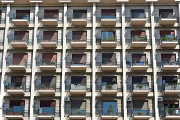 Mediterranean style multi story apartment building facade with rows of balconies and doors with shutters.