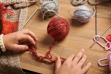 Child boy is learning to knit. Colorful wool yarns are on the wooden table. They are placed as...