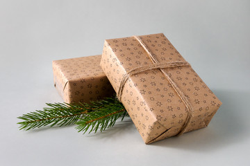 Christmas gifts wrapped in craft paper with twine and green spruce branches on grey background