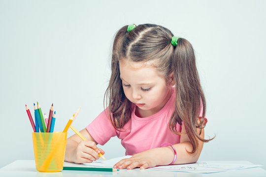 beautiful cute little girl drawing picture on white paper with colorful pencils