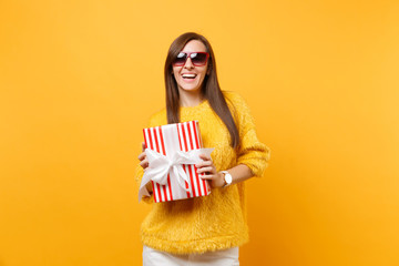 Portrait of laughing beautiful young woman in red eyeglasses holding red box with gift, present...
