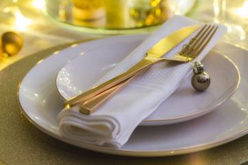 Christmas table setting with white plates and gold cutlery. Elegant festive dinner background with copy space. Xmas tableware background.