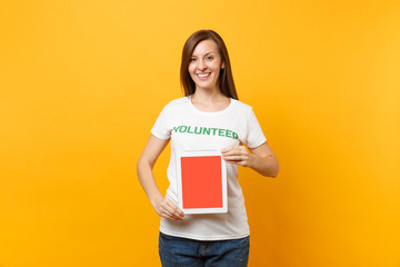 Woman in white t-shirt written inscription green title volunteer hold tablet pc computer, blank empty screen isolated on yellow background. Voluntary free assistance help, charity grace work concept.