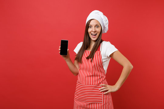 Housewife female chef cook or baker in striped apron white t-shirt toque chefs hat isolated on red wall background. Woman hold cellphone blank screen for promotional content Mock up copy space concept