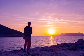 Silhouette of traveler who stands on the rock seashore