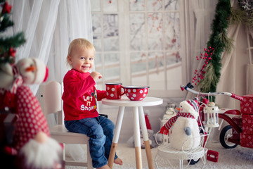 Naklejka premium Little toddler boy, drinking tea and eating cookies with plush toy on a snowy day
