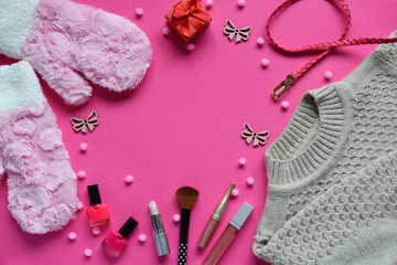 Knitted sweater, warm mittens, belt, nail polishes, lipstick on a pink background. Winter and autumn set of warm, comfortable clothes and makeup cosmetics. Copy space. Top view
