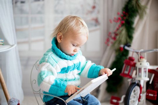 Cute little toddler child with colorful book at home on a snowy winter day