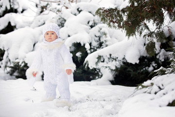 Cute little toddler boy, playing outdoors with snow on a winter day