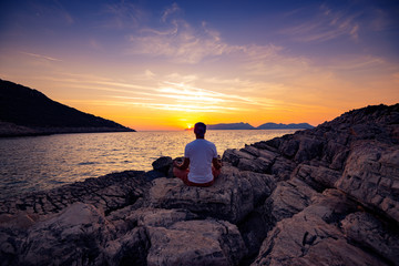 Traveler sits on the rock seashore and practicing yoga