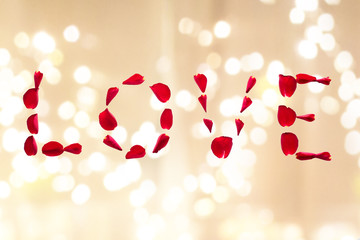 valentines day and romantic concept - word love made of red rose petals over festive lights background