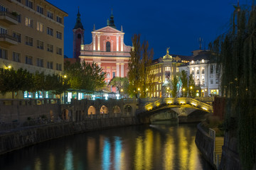 Fototapeta na wymiar Night time view of the center of Ljubljana featuring the lit up pink Franciscan church and the three way bridge 