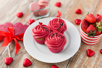 valentines day, sweets and romantic concept - close up of frosted cupcakes, red heart shaped chocolate candies, lollipops and strawberries