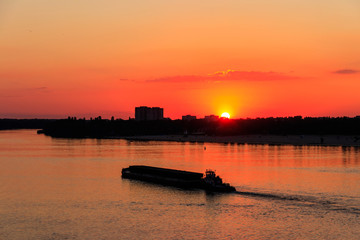 Tugboat pushing a heavy long barge on the river Dnieper at sunset