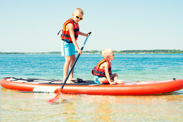 Two brothers swimming on stand up paddle board.Water sports , active lifestyle.	