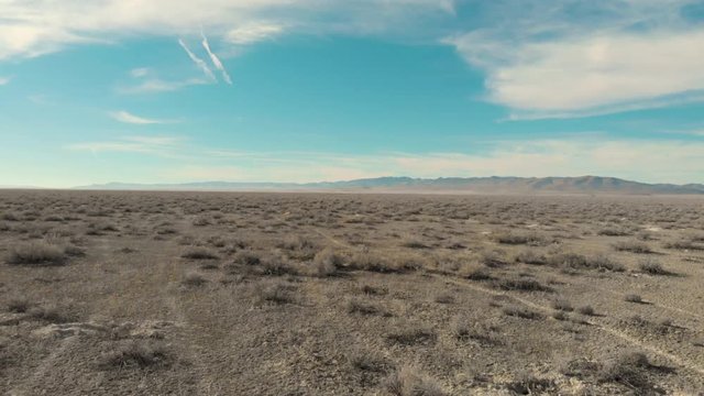 Aerial-Flying low over sparse desert vegetation toward distant mountains in the Great Basin Desert of Utah in the Western United States on a snowless winter day