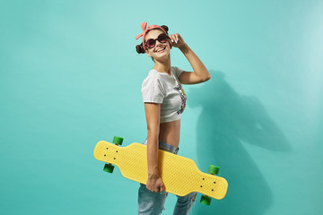 Funny young girl in sunglasses and pink bow on her head dressed in jeans and top stands with yellow...