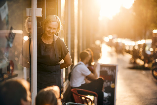 Smiling female owner standing at entrance of deli