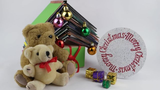 Two teddy bears with gifts sit on the background of the book composition in the form of a Christmas tree and rotating circle with the inscription Merry Christmas on the white background