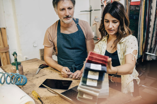 Female upholstery worker explaining male colleague over fabric swatch in workshop