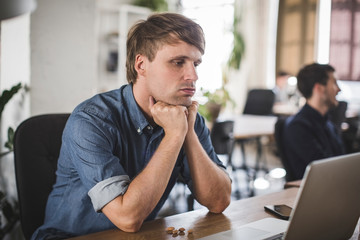 Tensed businessman looking at laptop while sitting at desk in creative office