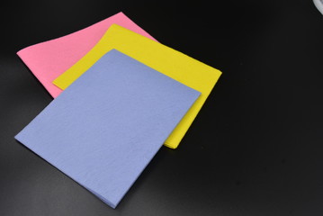 Colored new rags for dry and wet cleaning, yellow, purple and pink for the health and cleanliness of your home on a black matte background