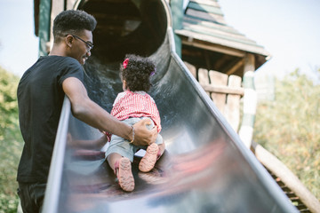 Father supporting daughter crawling up on slide at playground