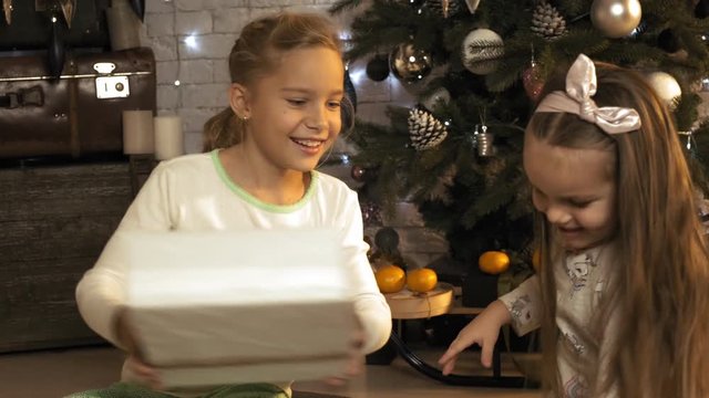 Children look with joy at New Year's gifts under the tree left by Santa in slow motion