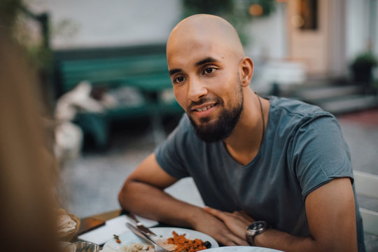 Smiling young man with shaved head looking at female friend during dinner party in backyard