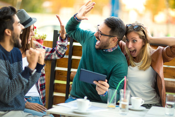 Group of four friends having a coffee together. Two women and two men at cafe talking laughing and enjoying their time using digital tablet.