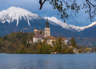 Fototapeta na wymiar Picture of Pilgrimage Church of the Assumption of Maria on an island on Lake Bled, Slovenia. Fall capture, with turning leaves framing the island and snow capped mountains
