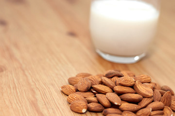 milk or almond drink in a glass with almonds and rustic wooden table background