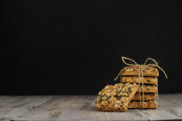 A stack of shortbread cookies with different types of nuts to a delicious coffee or tea on a dark wood table. horizontal view. black background. copy space. minimalism with baking.
