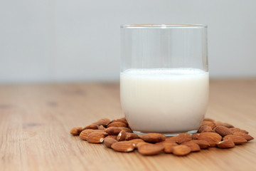 milk or almond drink in a glass with almonds and rustic wooden table background
