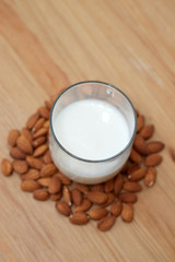 milk or almond drink in a glass with almonds and rustic wooden table background