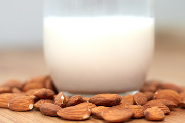 milk or almond drink in a glass with almonds and rustic wooden table background