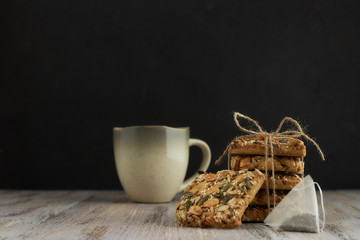A stack of shortbread cookies with different types of nuts to a delicious coffee or tea on a dark wood table. horizontal view. black background. copy space. minimalism with baking.