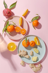 Fresh juicy tangerines, pomegranates and sliced fruits on colored plates on a pink background. Summer mood, healthy food. Top view.