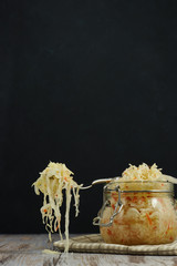 one jar of sauerkraut and carrots in its own juice with spices on a light, white wooden table, black background, horizontal view of the cabbage in the jar. traditional home-made,