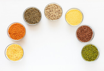 Flat lay glass bowls with superfoods are standing as arc on white background with copy space in middle. Stock of useful cereals for time of quarantine.